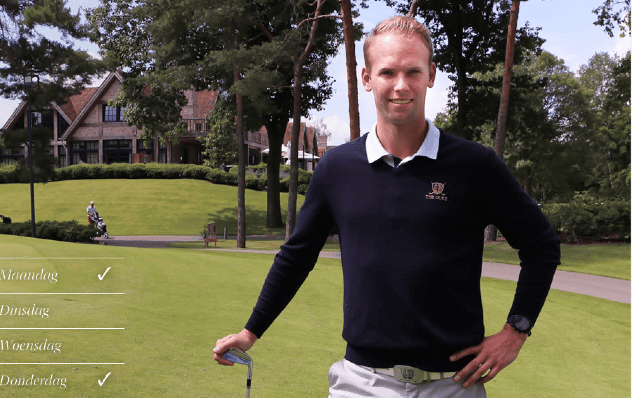 Patrick Goree met een golfclub op de golfbaan van The Duke, met bomen en het clubhouse op de achtergrond