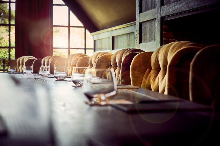 Lange vergadertafel met waterglazen en gestoffeerde stoelen in The Boardroom, met zonlicht door de ramen