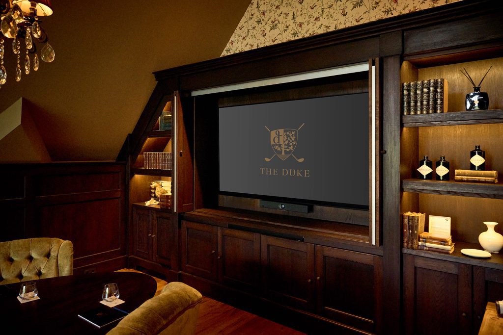 Scherm met het logo van The Duke in een donkere houten wandkast met boeken in The Boardroom