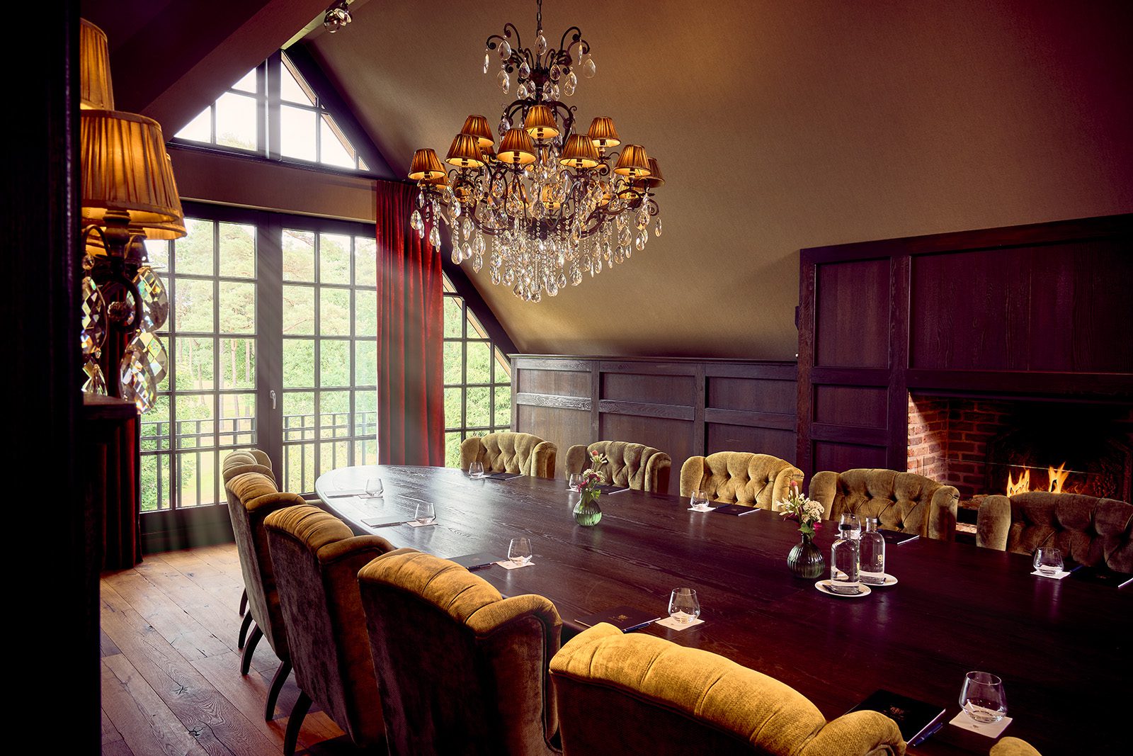 Lange vergadertafel met gestoffeerde stoelen, kroonluchter en brandende haard in The Boardroom van The Duke