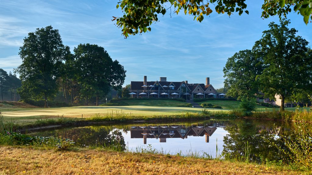 Het clubhouse van The Duke weerspiegelt in de vijver bij hole 18, met de green en bomen op de achtergrond
