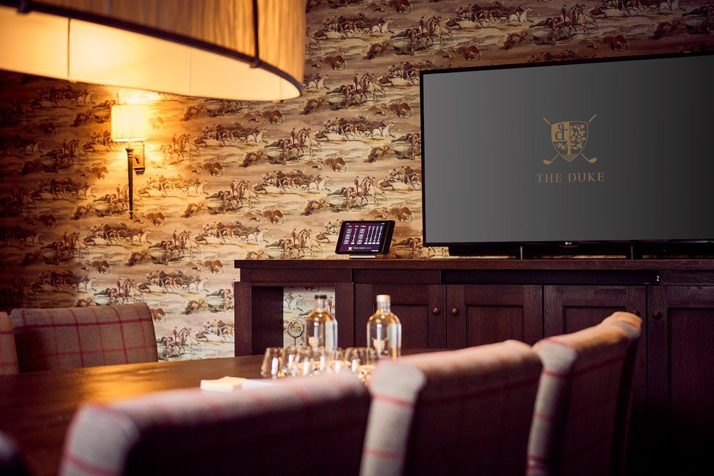 Vergadertafel met geruite stoelen, waterflessen en een scherm met het logo van The Duke in The Duke of York