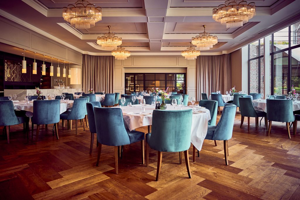 Gedekte ronde tafels met bloemen en blauwe stoelen onder kroonluchters in een zaal van The Royal Duke