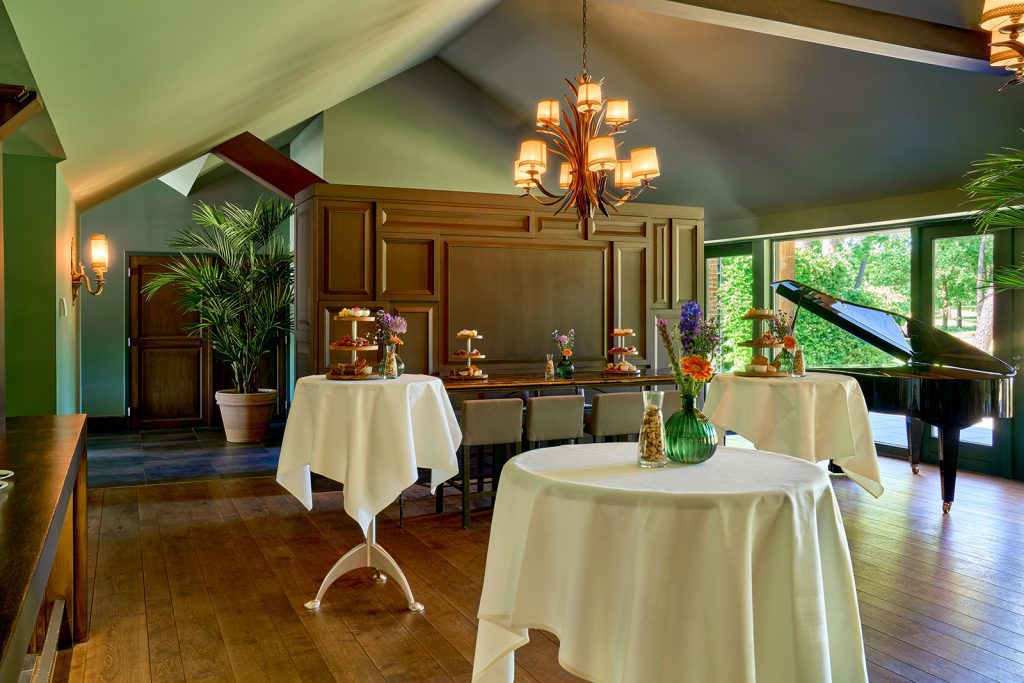 Statafels met witte kleden, bloemen en etagères met hapjes naast een vleugel in The Lodge