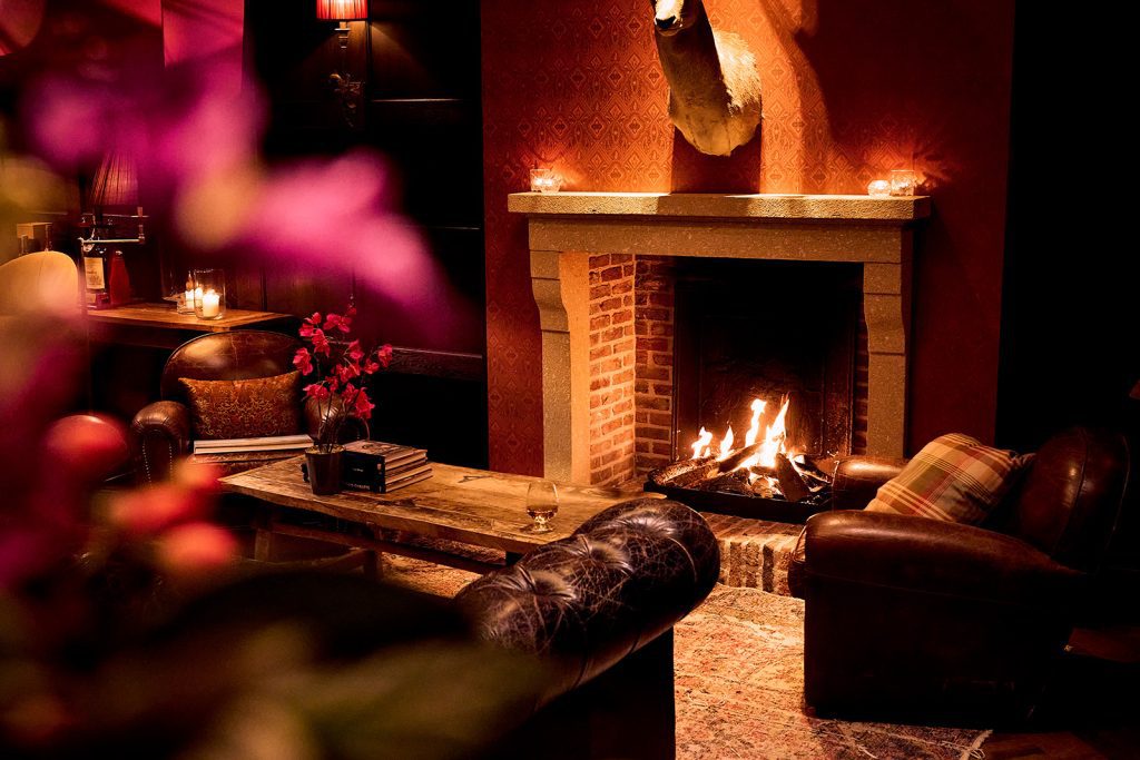 Leren fauteuils rond een houten tafel bij een brandende open haard in de Whiskeyroom van The Duke